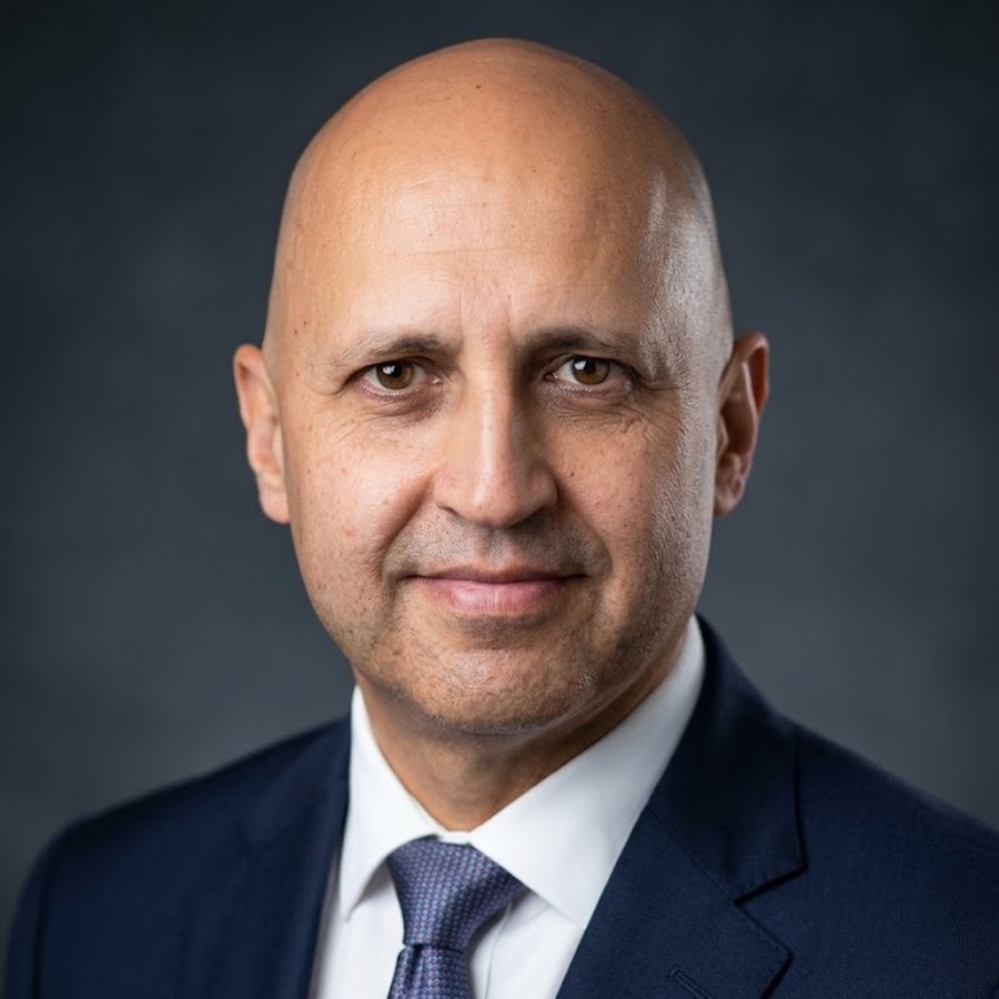 Professional headshot of Fabian de la Fuente wearing a navy plaid blazer and white shirt against a white background.